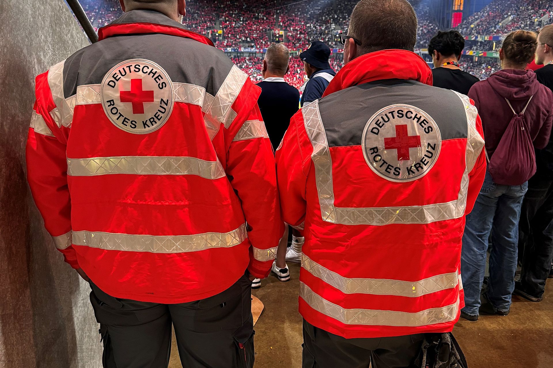 2 Sanitäter stehen mit dem Rücken zur Kamera und schauen auf das Spielfeld des Rhein Energie Stadions in Köln durch ein Mundloch im Oberrang